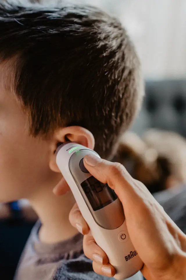 Kid getting temperature taken with ear thermometer while having stomach flu
